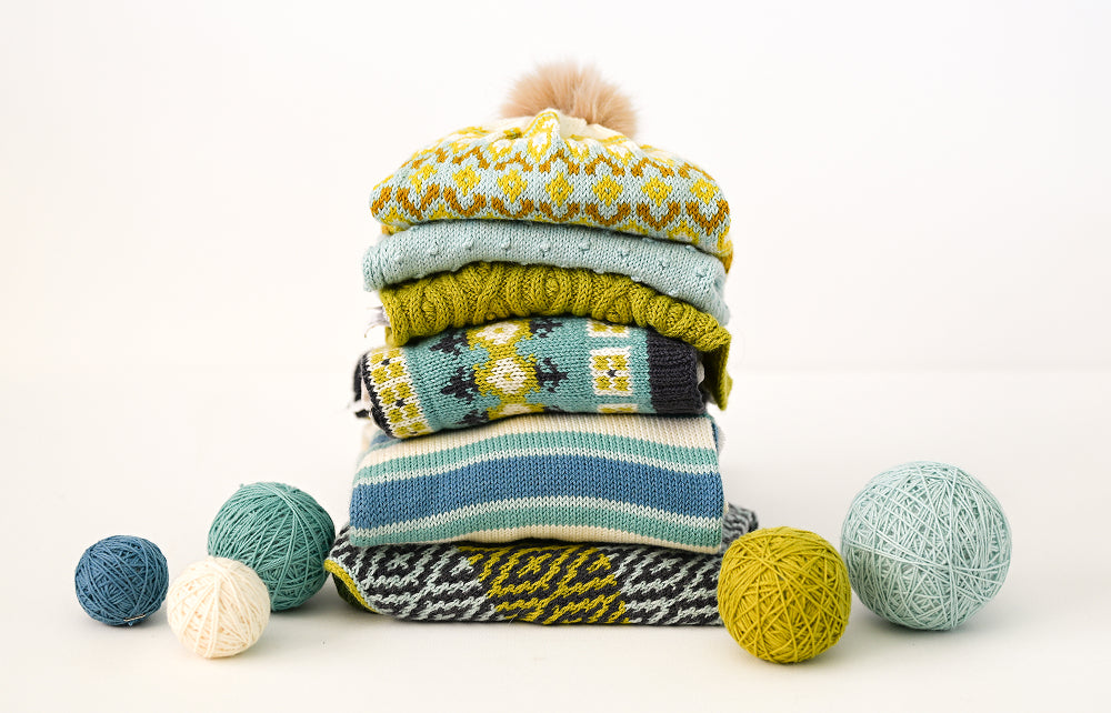 Stack of colorful knitted sweaters with yarn balls on a white background
